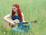 Old Bus Depot Markets Busker, Georgia Bennett siting with her guitar in a meadow